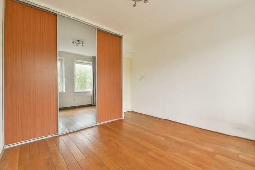 A spacious minimalist room featuring a large mirrored wardrobe and warm wooden flooring. The natural light filters through the window, creating a serene atmosphere.