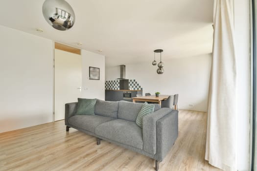 Stylish living room featuring a grey striped sofa with green cushions, a sleek kitchen in the background, and modern lighting fixtures, creating a contemporary ambiance.