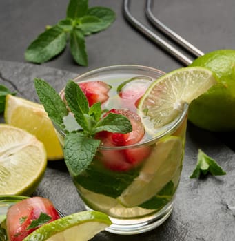 Refreshing mojito cocktail with lime, mint, strawberry, and ice on dark background