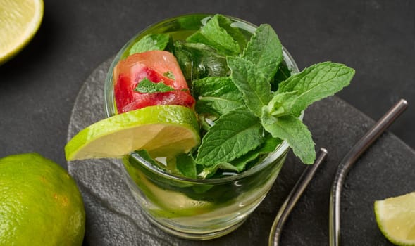 Refreshing mojito cocktail with lime, mint, strawberry, and ice on dark background, top view