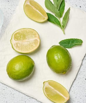 A minimalist composition featuring green whole limes and a juicy halved lime paired with a tied sprig of fragrant mint leaves