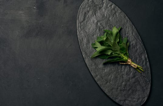 A small bunch of fresh green mint sprigs tied with brown twine rests on an empty, textured black oval plate. Copy space