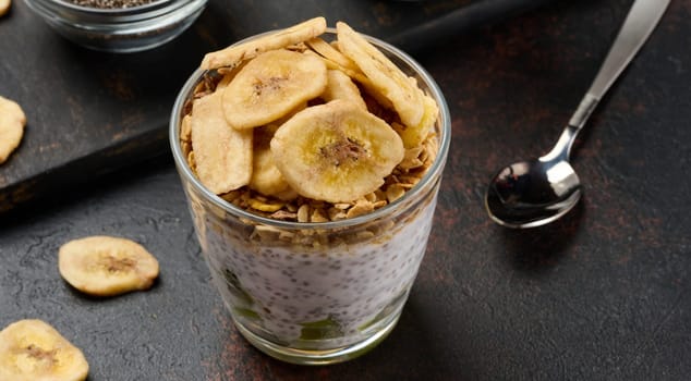 Glass of chia seed pudding layered with kiwi, topped with granola and banana chips, top view