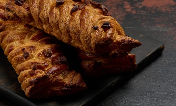 Golden brown maple pecan braid pastries are arranged on a dark, textured surface. Braided dough is flaky and topped with pecans