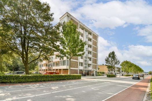 A contemporary multi-story residential building is set against a backdrop of leafy trees and a clear sky, creating a serene neighborhood atmosphere.