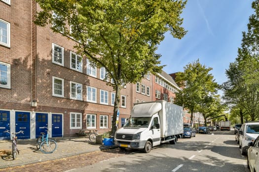 A scenic street featuring a mix of modern and historic buildings, lined with trees and parked vehicles, showcasing urban life and architecture.