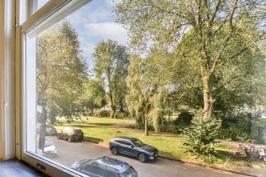 A serene view captured from a window, showcasing lush green trees and parked cars in a peaceful public park setting.