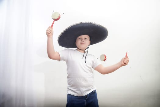 A young boy joyfully engages in a cultural celebration, wearing a traditional sombrero and holding maracas to make music.