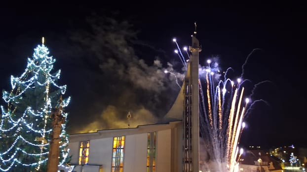 Fireworks during Christmas. View of the illuminated Christmas tree and fireworks over the church in the town.