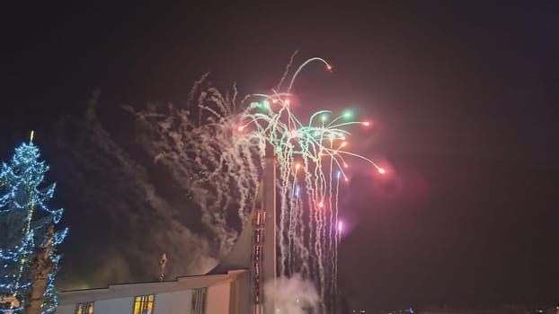 Fireworks during Christmas. View of the decorated Christmas lighted tree and fireworks over the church in the town.
