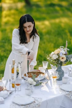 A woman is wearing a beautiful white dress and she is skillfully cutting a pie on a table that is welldecorated with charming items