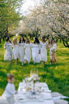 A lovely group of women is gracefully walking in the park while wearing elegant white dresses that enhance the beauty of the setting