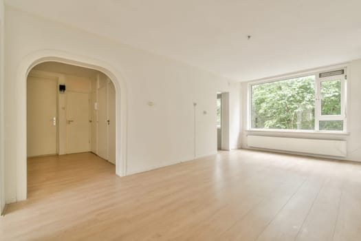 A spacious, minimalist room featuring wooden floors and large windows that allow ample natural light, creating a bright atmosphere.