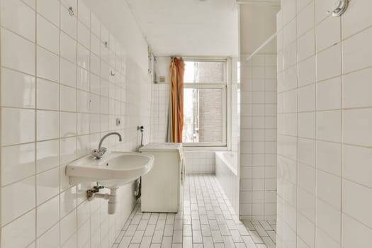 A spacious, minimalist bathroom featuring white tiles, a simple sink, and a freestanding bathtub illuminated by natural light from a window.
