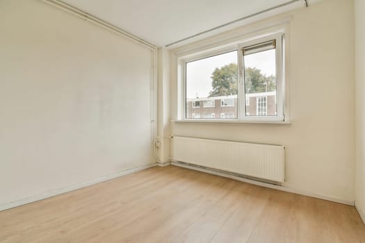 An empty room featuring a large window that offers natural light, showcasing the simplicity of indoor space with neutral tones.
