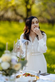 A woman elegantly dressed in a flowing white dress is seated at a table, savoring a delightful piece of cake, enjoying her moment