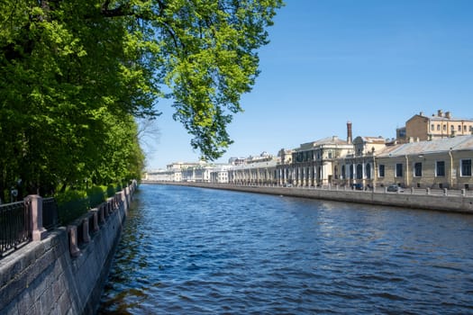 Saint-Petersburg, Russia - 05.21.24. Urban riverside scene captures a serene Fontanka river lined with historic architecture and lush greenery under a clear sky