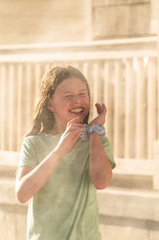 A joyful young girl gleefully gets soaked in refreshing water mist during a hot summer day.