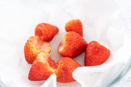 Freshly washed and dried strawberries are carefully arranged in a glass bowl lined with paper towel, ready for snacking or further use.