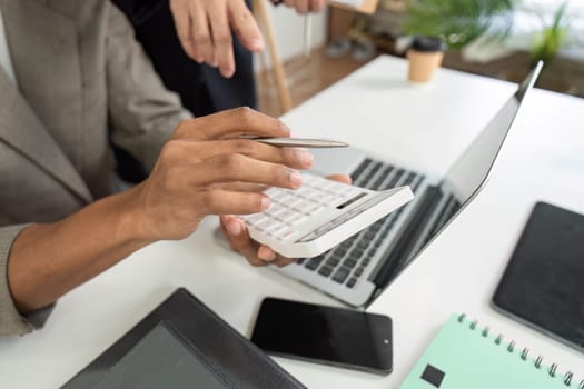 In a collaborative office environment, a professional uses a calculator to analyze data while discussing insights with a colleague, showcasing teamwork.