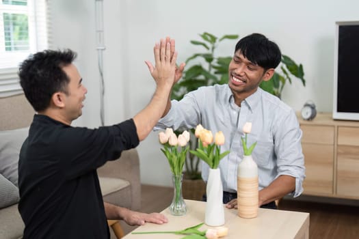 Two friends engage in a playful high-five, surrounded by flowers, symbolizing their friendship and connection in a warm and inviting space.