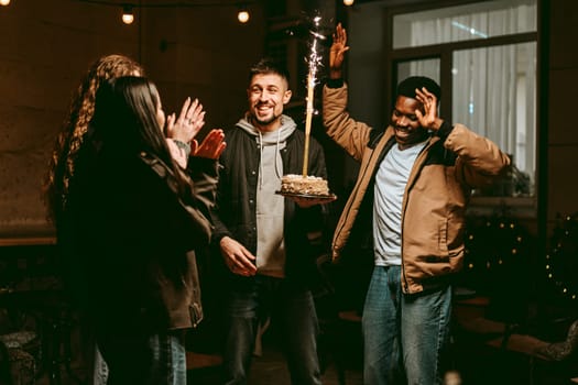 Friends gather in a cozy night setting, celebrating a special occasion as one person holds a birthday cake adorned with sparklers. Laughter and cheers fill the air.