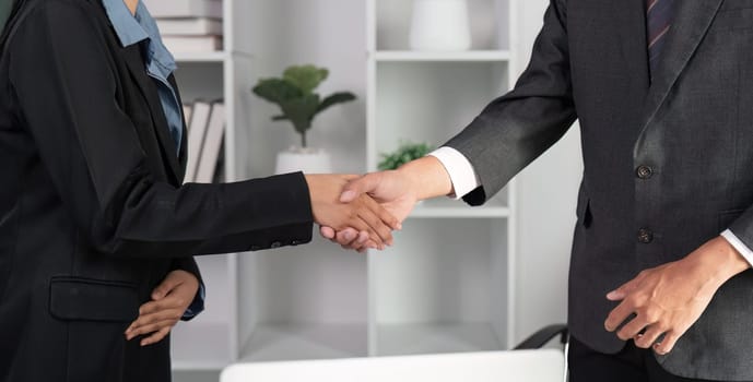 Two businessmen shake hands in a modern office, celebrating a successful collaboration and achievement.