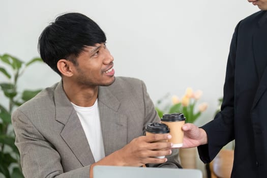 During a business meeting, two men exchange coffee cups while discussing important project details, showcasing a friendly professional rapport.