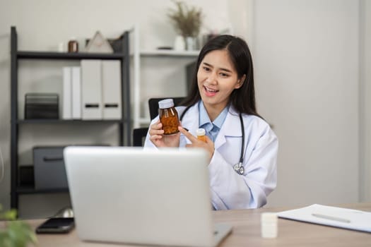 A confident female doctor conducts an online consultation, showcasing a medicine bottle in a modern medical office setting.