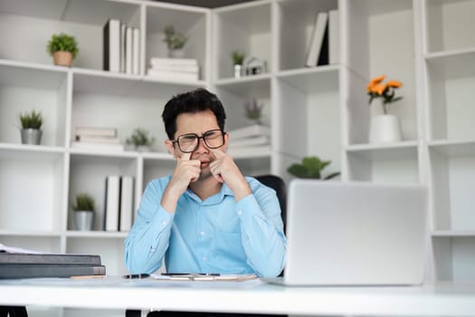 Office worker feeling overwhelmed and tired, suffering from a headache due to a demanding work schedule in a contemporary office setting.