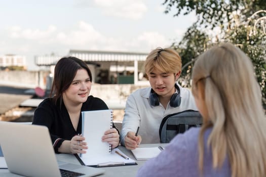 Young students collaborate outdoors, using laptops and notebooks, fostering teamwork and learning in a modern educational environment.