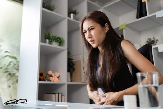 A businesswoman experiencing discomfort while working in a contemporary office setting, highlighting workplace health challenges.