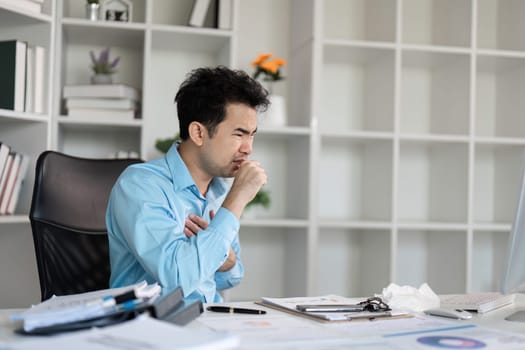 An office worker sits at their desk, visibly unwell with a cold, surrounded by work materials in a modern office setting.