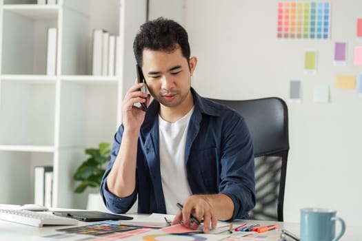 Graphic designer in a studio setting, surrounded by design tools and color samples, focused on creative work.
