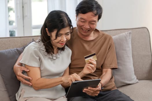 Senior couple happily shopping online with a tablet and credit card, enjoying modern technology in a comfortable home environment.