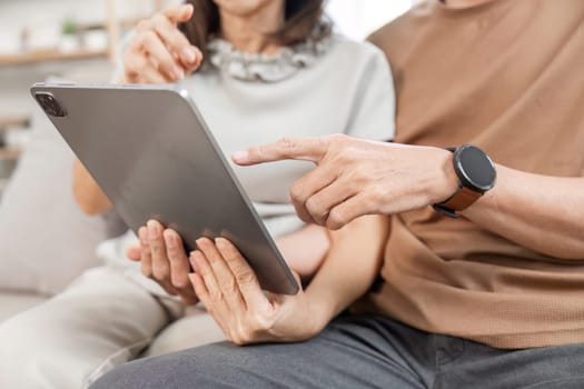 Elderly couple sitting on a sofa, using a tablet, enjoying a peaceful and relaxing moment in their cozy living room.