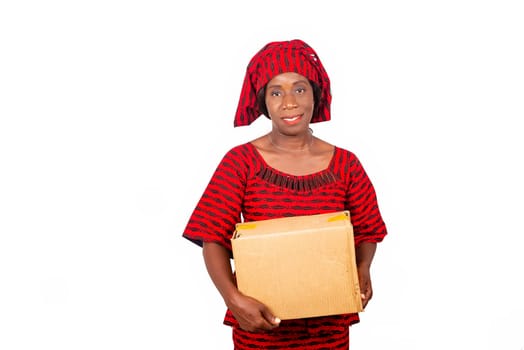 beautiful african adult woman dressed in red loincloth standing holding a cardboard box smiling. isolated on white background
