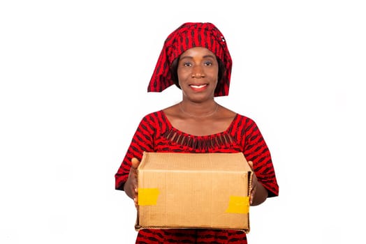 beautiful african adult woman dressed in red loincloth standing holding a cardboard box smiling. isolated on white background