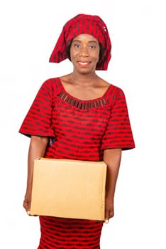 beautiful African mature woman standing and dressed in red loincloth suit holding a cardboard box in hand while being happy. White background