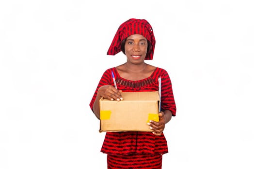 beautiful african adult woman dressed in red loincloth standing holding a cardboard box; a pen, document in hand on white isolated background