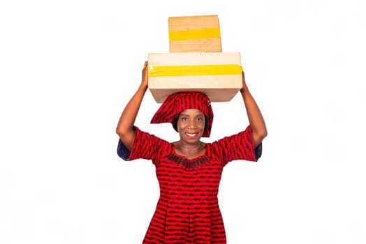 beautiful african adult woman dressed in red loincloth standing holding boxes of cardboard on the head being happy. isolated on white background