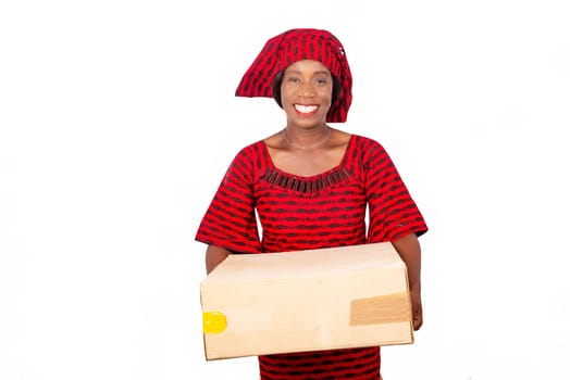 beautiful african mature woman standing and dressed in red loincloth suit holding a cardboard box in hand while being happy