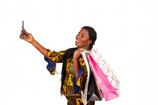 Happy beautiful adult woman standing with shopping bags and taking selfie on her mobile phone on white background