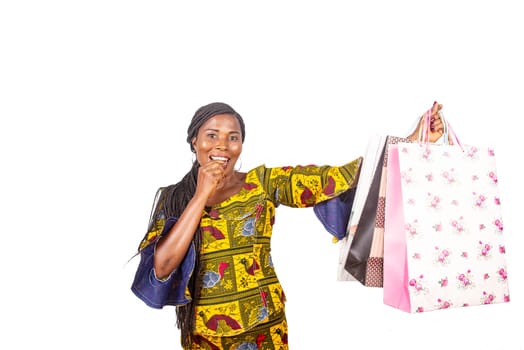 beautiful adult woman dressed in African loincloth with braided hair holding several shopping bags making a gesture of victory. White background