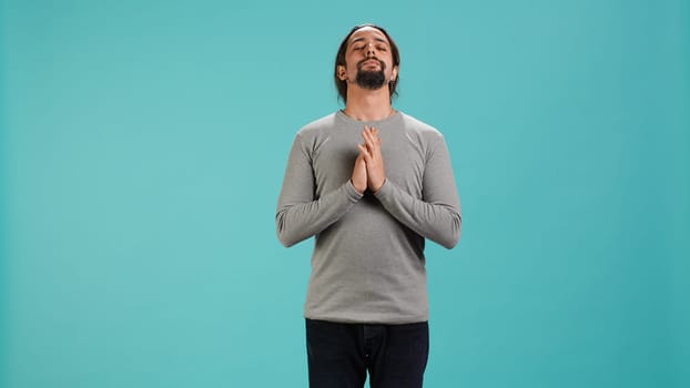 Relaxed man looking up to sky, closing eyes, waiting for sign from his god. Zen spiritual man doing worship hand gesturing, hoping for miracle, isolated over studio background, camera A