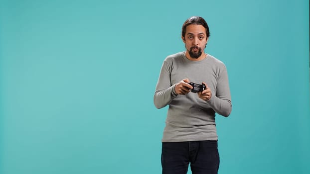 Gamer with disappointed look on face after receiving game over screen, holding controller. Man upset after losing videogame, playing with gamepad, isolated over studio background, camera A