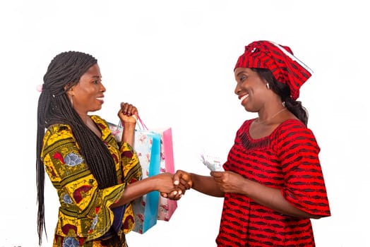 Two beautiful businesswomen standing in traditional outfit on white background shake hands smiling after shopping.