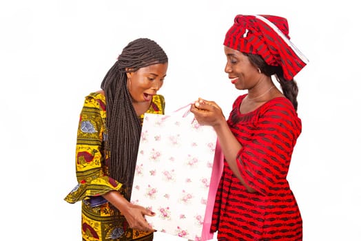 Two beautiful african women standing in traditional  outfit looking in bags of surprise shopping.