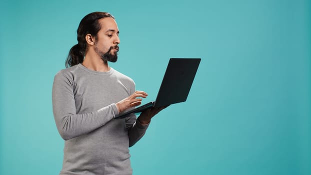 Portrait of smiling person spending time on laptop, isolated over studio background. Cheerful man checking social media posts on notebook, enjoying leisure time, camera B