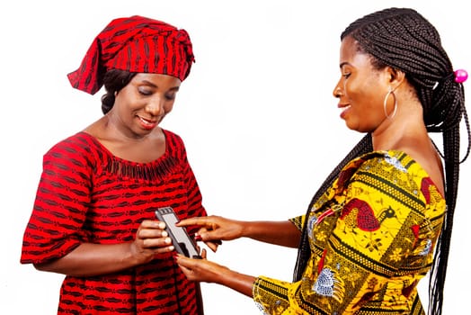 Two beautiful women in traditional clothes standing on white background showing a mobile phone while smiling.